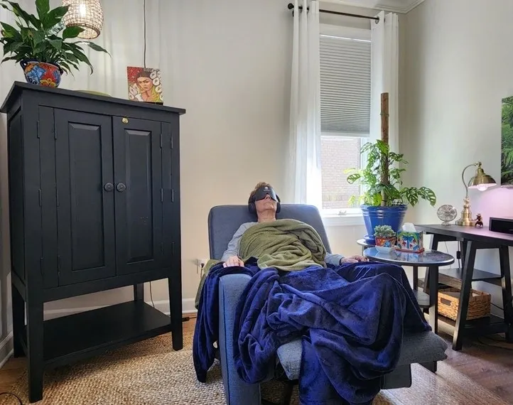 Person relaxing on a chair covered with blankets in a cozy room.